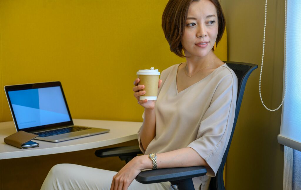 Woman sitting at desk with laptop and coffee, enjoying a relaxed moment during work.